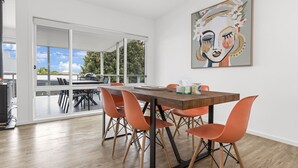 A modern dining area with a wooden table and orange chairs, a large window with a view of the outdoors, and a piece of abstract art on the wall.