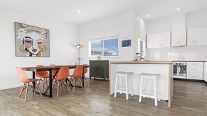 A modern kitchen with white cabinets, a wooden dining table with orange chairs, and a small island with stools.
