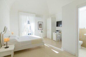 Habitación de hotel con cama, mesita de noche con lámpara, escritorio con silla, televisor montado en la pared y baño con inodoro y lavamanos.