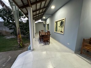 A covered patio area with a dining table and chairs, a large window, and a potted plant. - BEACH HOUSE (Prado)