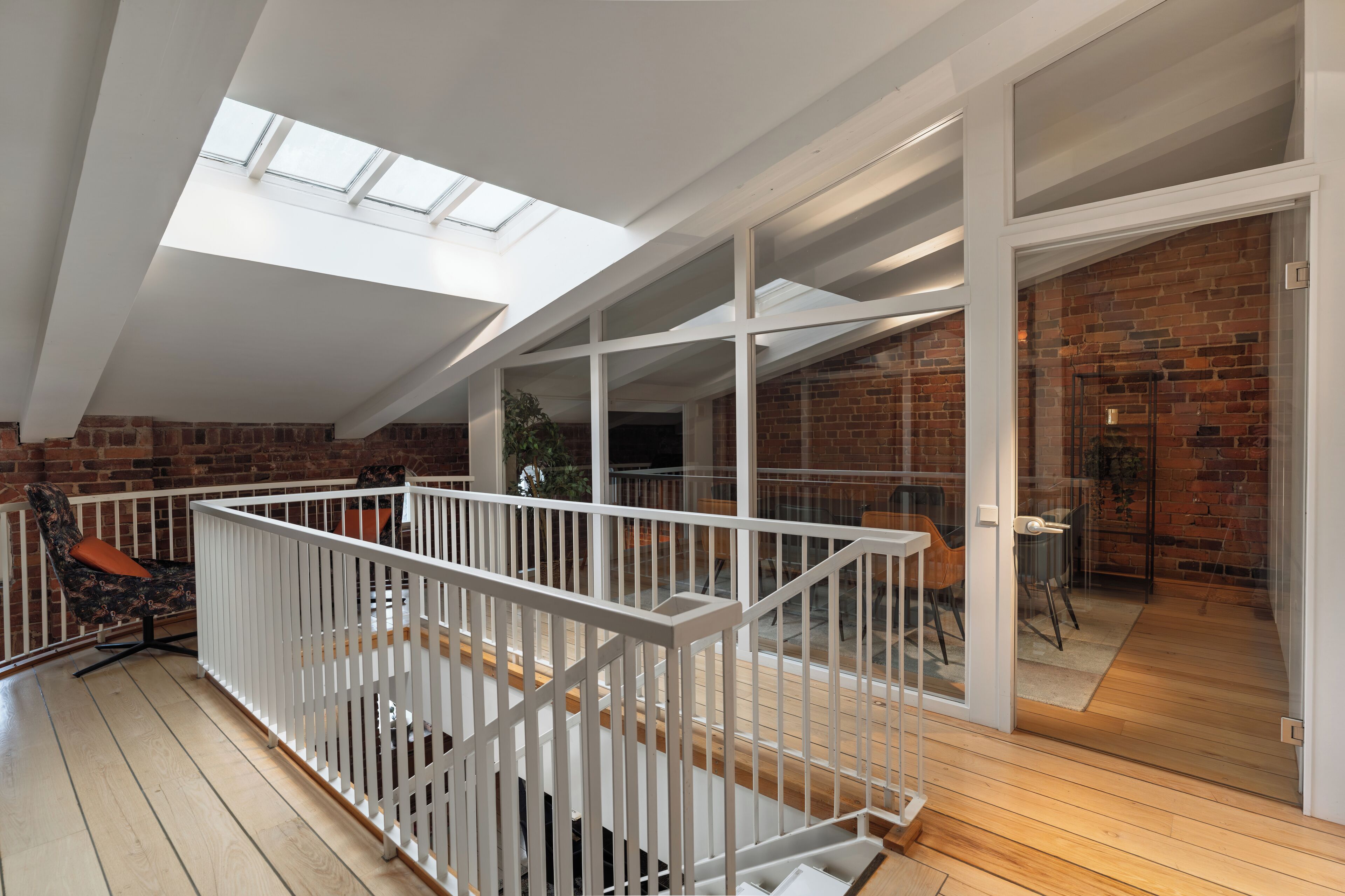 A spacious loft with a high ceiling, skylights, a wooden floor, and a brick wall.