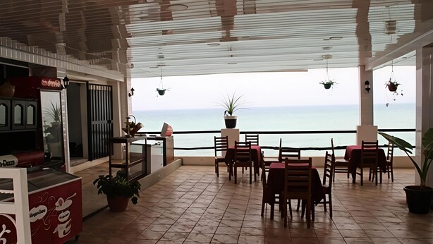 En restaurang med uteservering och utsikt över havet, med ett klinkergolv och bord och stolar i trä.