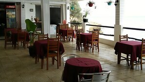 En restaurang med träbord och stolar, ett kylskåp och hängande växter.