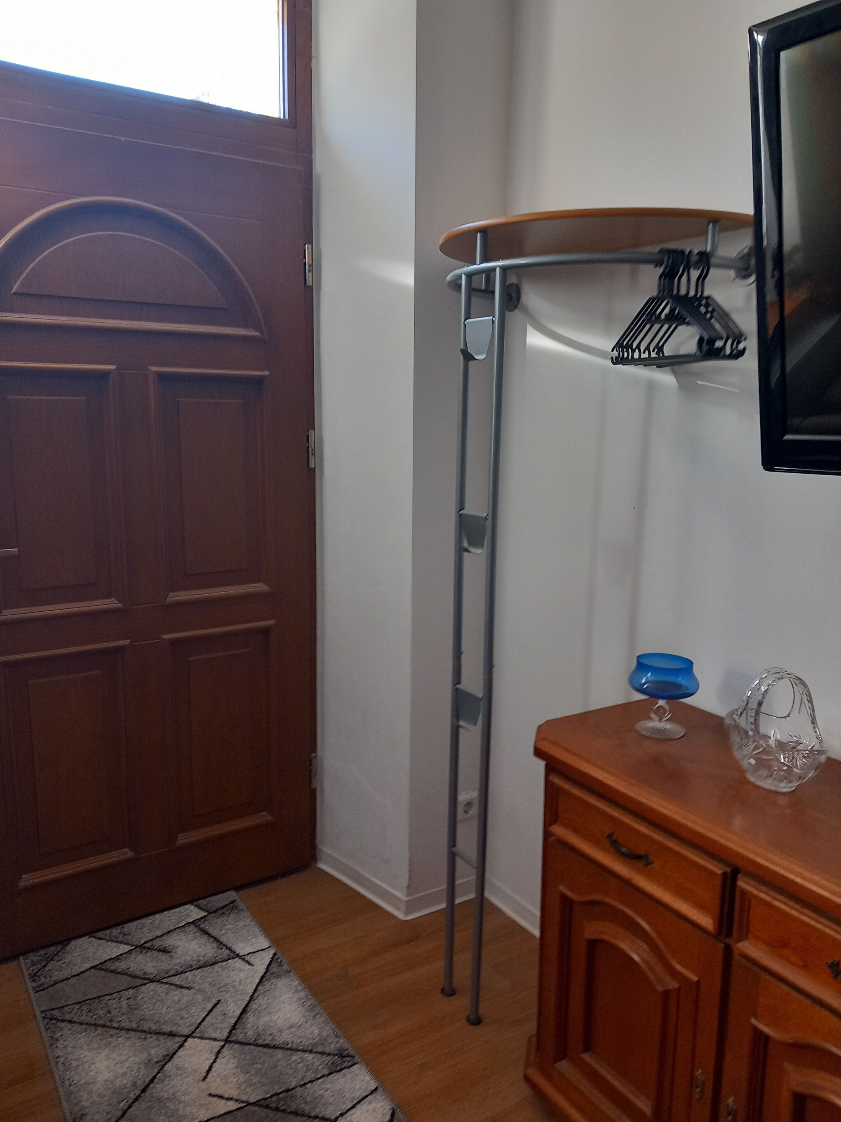 Una habitación con una puerta de madera, una escalera de metal, un aparador de madera y un pequeño cuenco azul sobre el aparador.