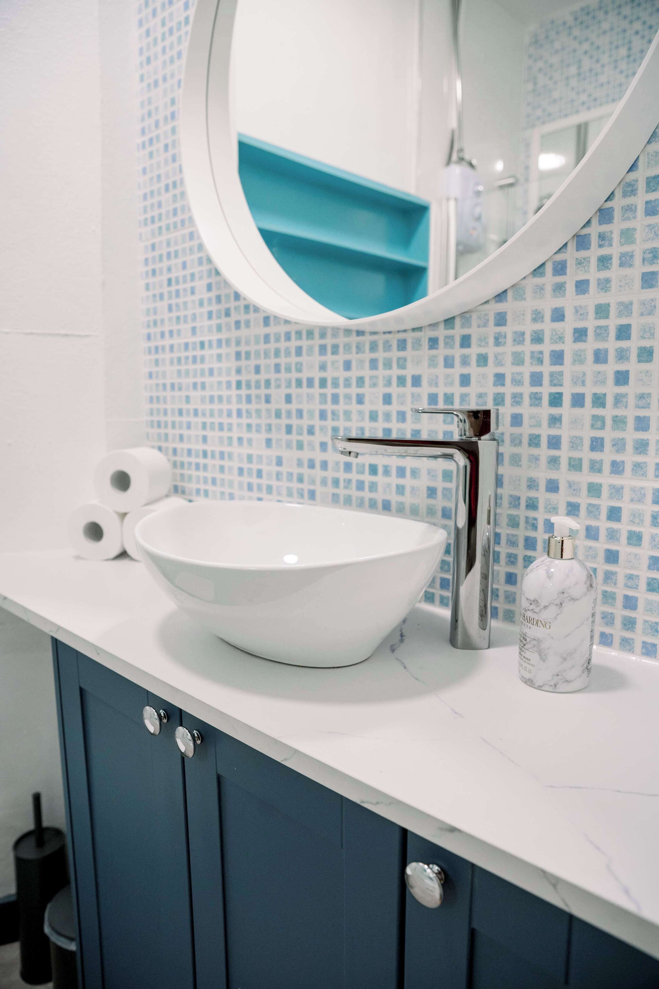 A bathroom with a white sink, blue cabinets, and a mirror with a blue backsplash.
