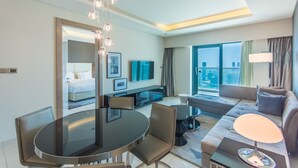 A modern hotel room with a dining area, a sofa, a TV, and a large window offering a city view. - Spacious 1BR Rental | 1050 sq ft | Luxury Lifestyle in Paramount Towers (Dubai)