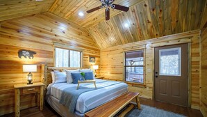 Ein Schlafzimmer einer Holzhütte mit Bett, Nachttisch, Lampe, Bank und Fenstern.