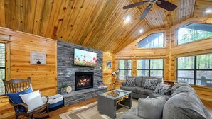 Ein Blockhaus-Interieur mit Kamin aus Naturstein, Holzwänden, einer Couch und einem Schaukelstuhl.
