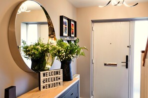 A reception area with a mirror, two potted plants, a welcome sign, and a door. - South Beach House (Blyth)