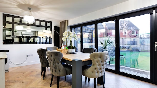 A dining area with a wooden table and tufted chairs, a large mirror, and a view of a backyard through a sliding glass door.