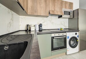 A compact kitchen with a built-in oven, microwave, and washing machine. - Paceville Energy Meets Comfort, 2BR Apt + Balcony! (St. Julian`s)