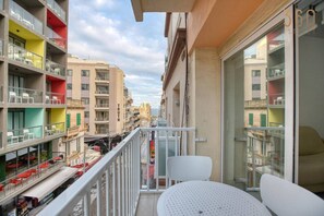 Ein Balkon mit weißen Stühlen und einem Tisch, mit Blick auf eine Straße mit bunten Gebäuden und einem Restaurant darunter.