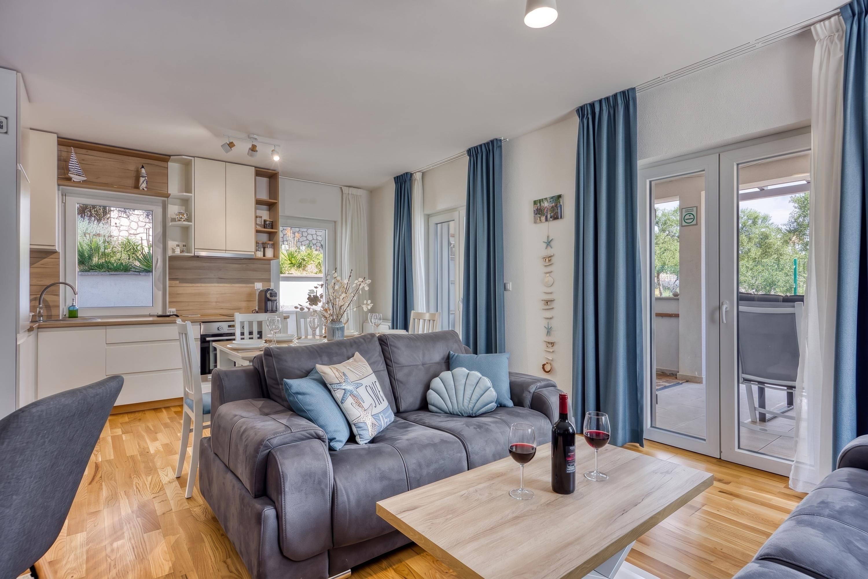 A modern living room with a grey sofa, a wooden coffee table, and a dining area with a white table and chairs.