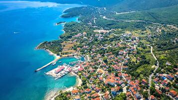 An aerial view of a coastal town with a marina, residential areas, and surrounding hills.