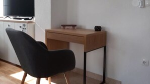 Une petite pièce moderne, dotée d’un bureau en bois, d’une chaise noire, d’un téléviseur et d’un symbole Wi-Fi sur le meuble.