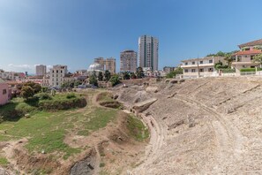 Un vaste amphithéâtre en plein air, doté d’une scène en terre et d’un espace réservé aux spectateurs, entouré de bâtiments modernes et de verdure.