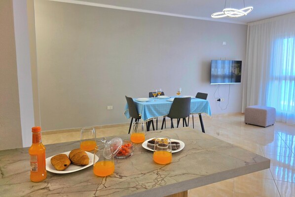 Comedor con una mesa de mármol, alimentos para el desayuno y un televisor en la pared.