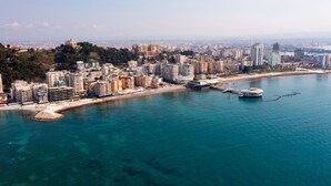 Un paysage urbain côtier avec un port de plaisance, des immeubles de grande hauteur et un bâtiment remarquable situé au sommet d’une colline.