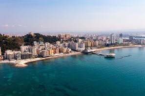 Un paysage urbain côtier avec un port de plaisance, des immeubles de grande hauteur et un bâtiment remarquable situé au sommet d’une colline.