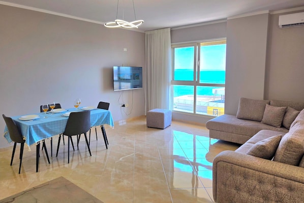 Una sala de estar moderna con comedor, televisor de pantalla plana, ventana grande con vistas y sofá gris.