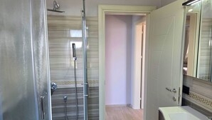 Egy fürdőszoba üveg válaszfallal ellátott zuhanyzóval, fehér mosdókagylóval és tükörrel.