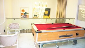 Une table de billard dans une pièce dotée d’une rambarde en verre, d’un fauteuil rembourré et d’œuvres d’art accrochées au mur.