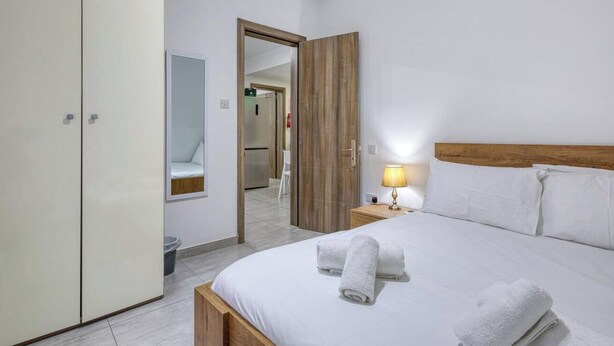 Ein Hotelzimmer mit Bett, Holz-Kopfteil, Nachttisch mit Lampe, Schrank und Spiegel.