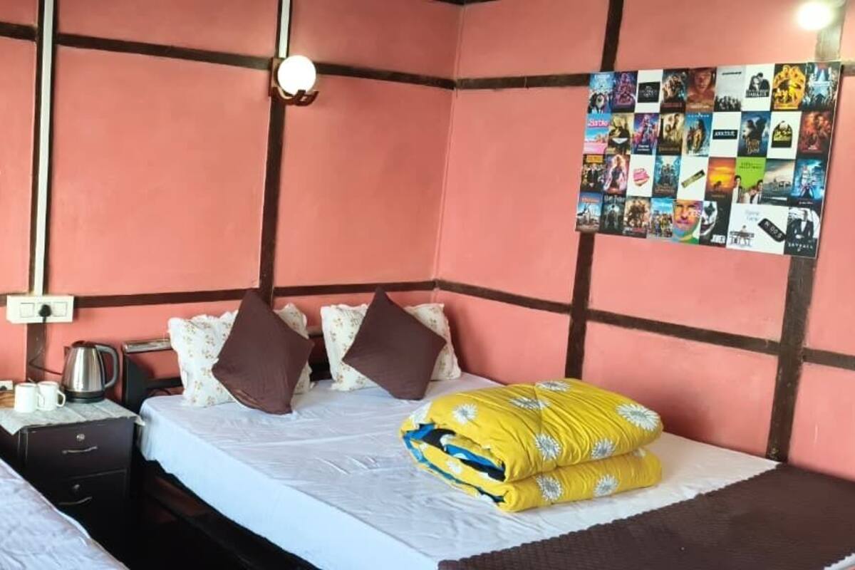 A room with two beds, a nightstand, a kettle, and a wall with movie posters.