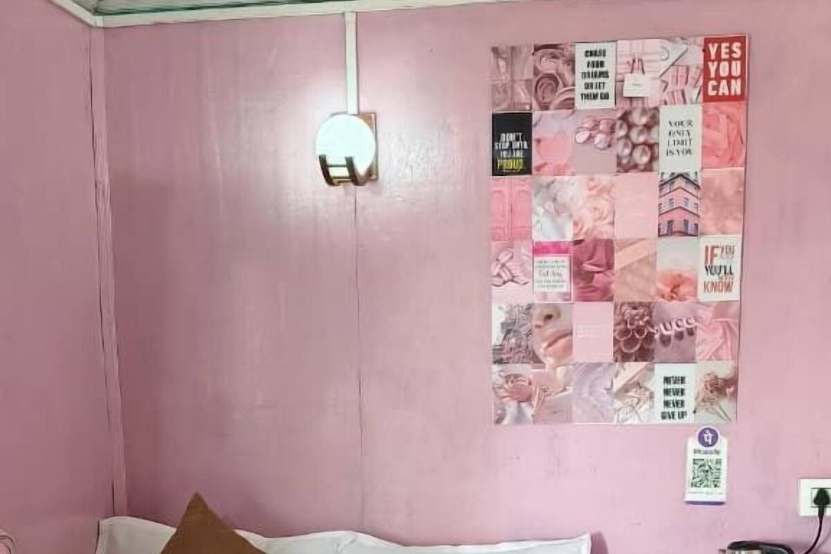 A bedroom with a bed, pillows, a wooden nightstand, a wall poster, and a red-framed window.