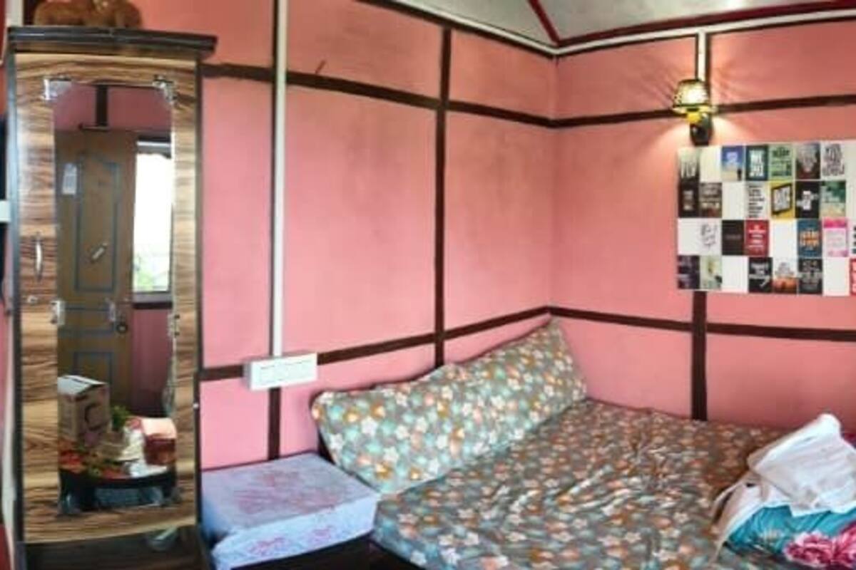 A room with a bed, bedside table, and a mirror. There is a wall with a bulletin board and a shelf with various items.