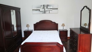 Un dormitorio con una cama de madera, dos mesitas de noche con lámparas, un aparador y un cuadro abstracto grande en la pared.