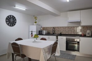 A compact kitchen with white cabinets, a microwave, an oven, and a clock on the wall. - Fifty's House 2 By Sam Houses (Tabua)