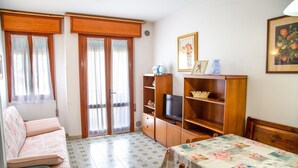 Una sala de estar acogedora con un sofá, televisión, estanterías de madera y una mesa de comedor.