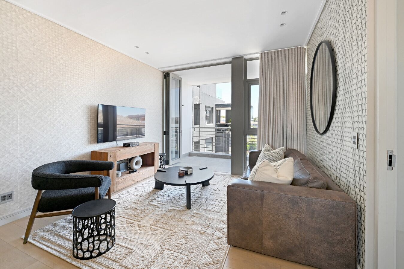 Een moderne woonkamer met een bank, een bijzettafeltje, een televisie en een kamerkleed met een patroon.