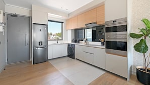 A modern kitchen with stainless steel appliances, a built-in washing machine, and a large window providing natural light. - Quiet 2-bed Green Point Retreat Rooftop Pool (Cape Town)