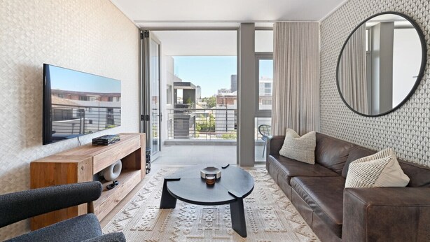 A modern living room with a flat-screen TV, a wooden console table, a brown leather sofa, and a round mirror. - Quiet 2-bed Green Point Retreat Rooftop Pool (Cape Town)