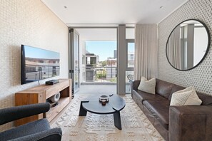 Un salon moderne avec un téléviseur à écran plat, une console en bois, un canapé en cuir marron et un miroir rond.