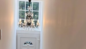Un couloir avec une porte blanche, une fenêtre au-dessus et un lustre.