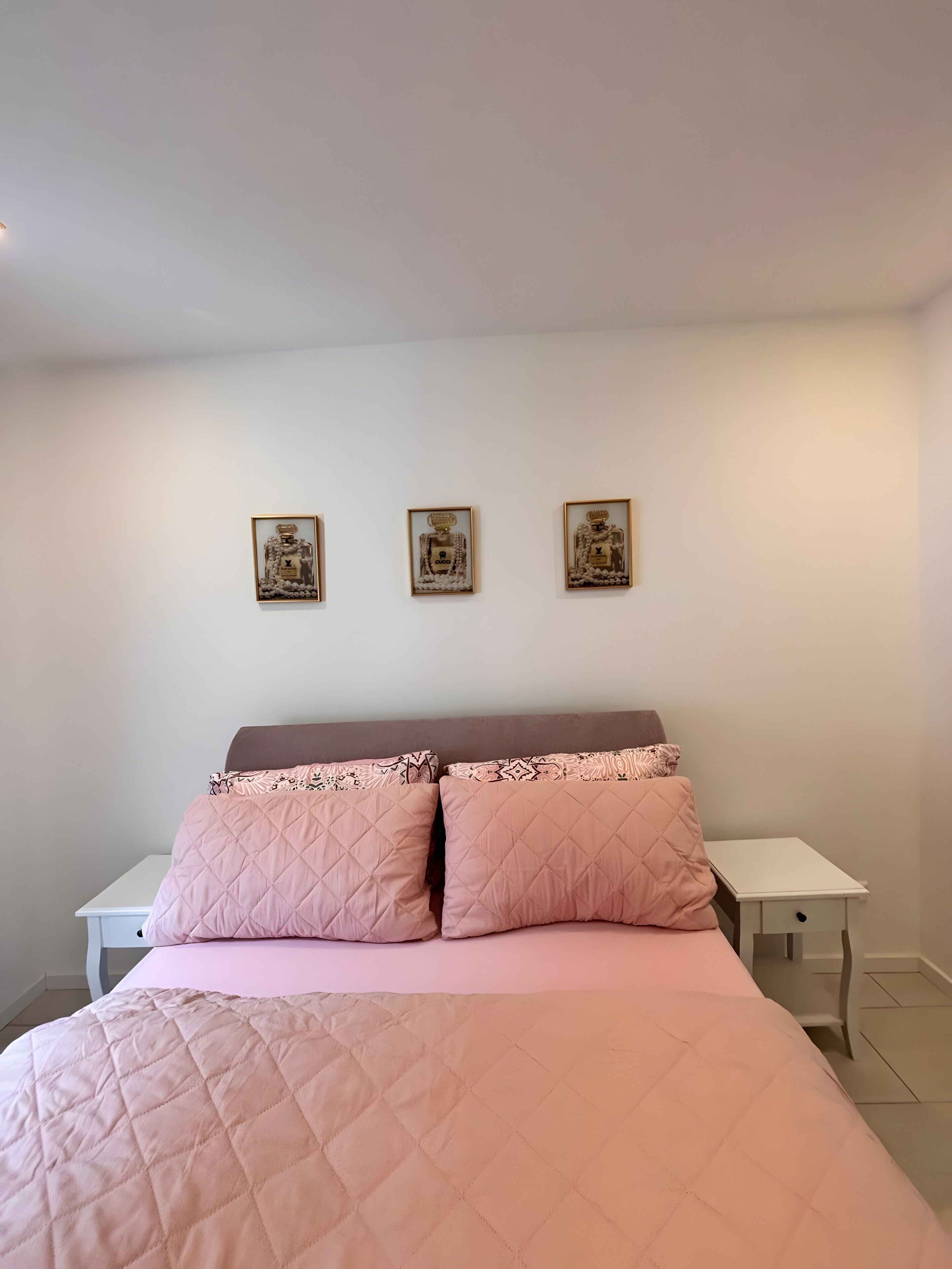 A bedroom with a bed, two bedside tables, and three framed pictures on the wall.