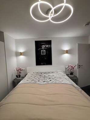 Une chambre à coucher moderne avec un grand lit, deux tables de chevet avec des lampes, une affiche encadrée au mur et une porte.