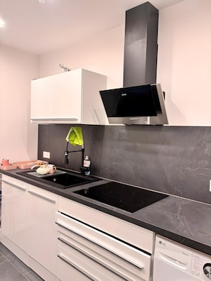 Une cuisine moderne dotée d’une plaque de cuisson noire, de meubles blancs, d’un four à micro-ondes et d’un lave-vaisselle.