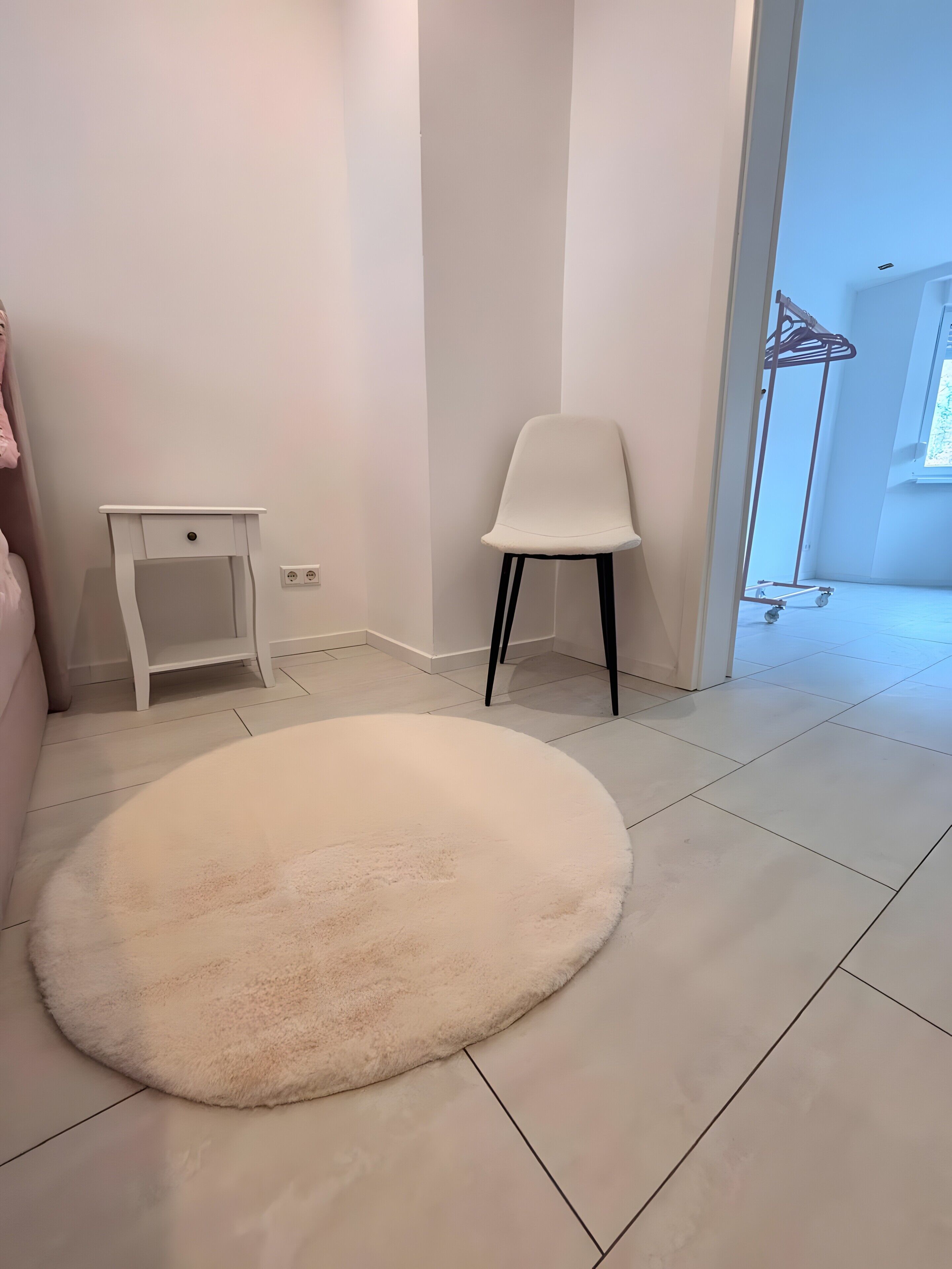 A room with a white floor, a white chair, a small white table, and a fluffy white rug.