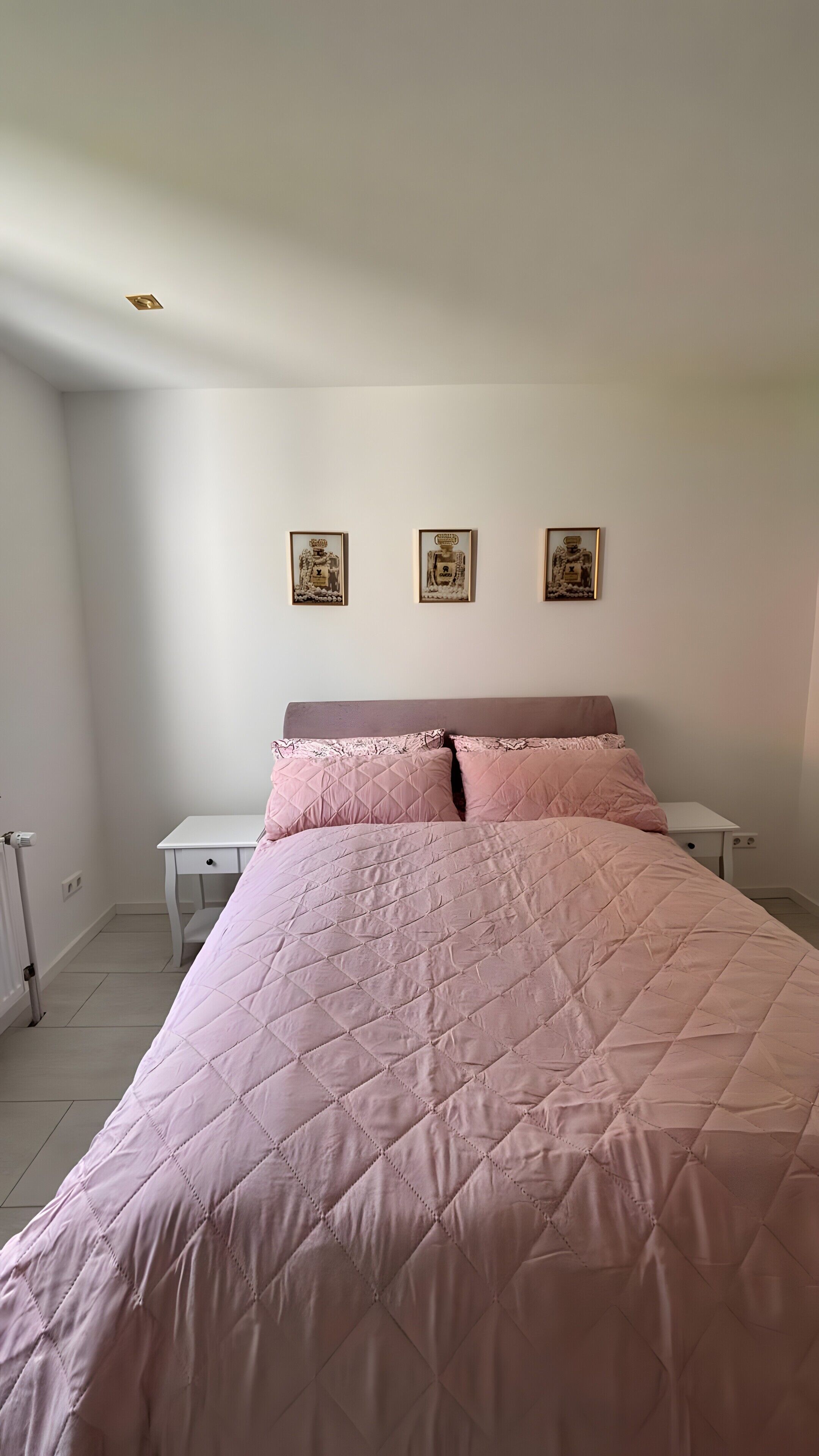 A bedroom with a bed, two bedside tables, and three wall-mounted pictures.