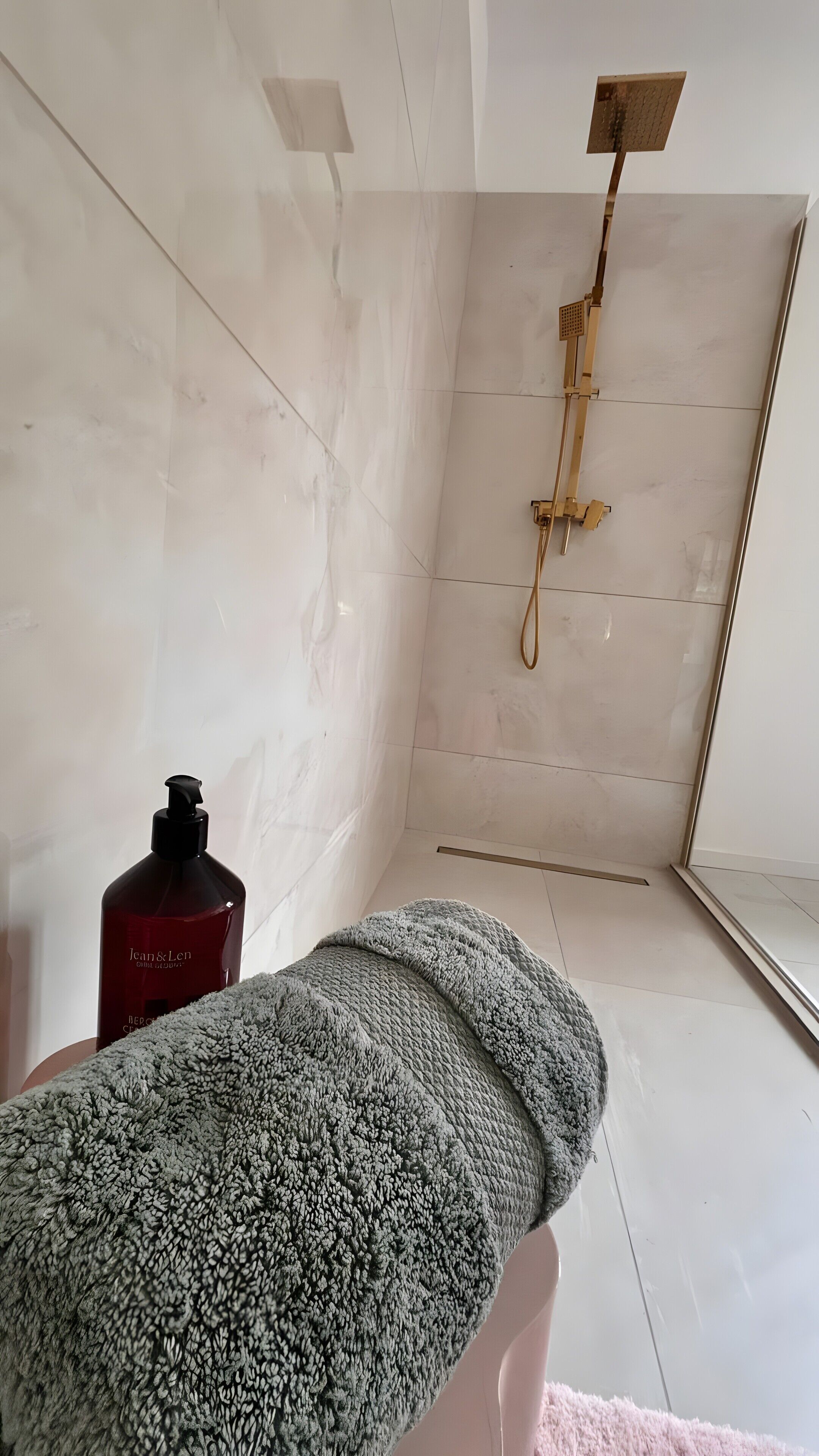 A bathroom with a shower, a bottle of Jean & Len body lotion, and a fluffy towel.