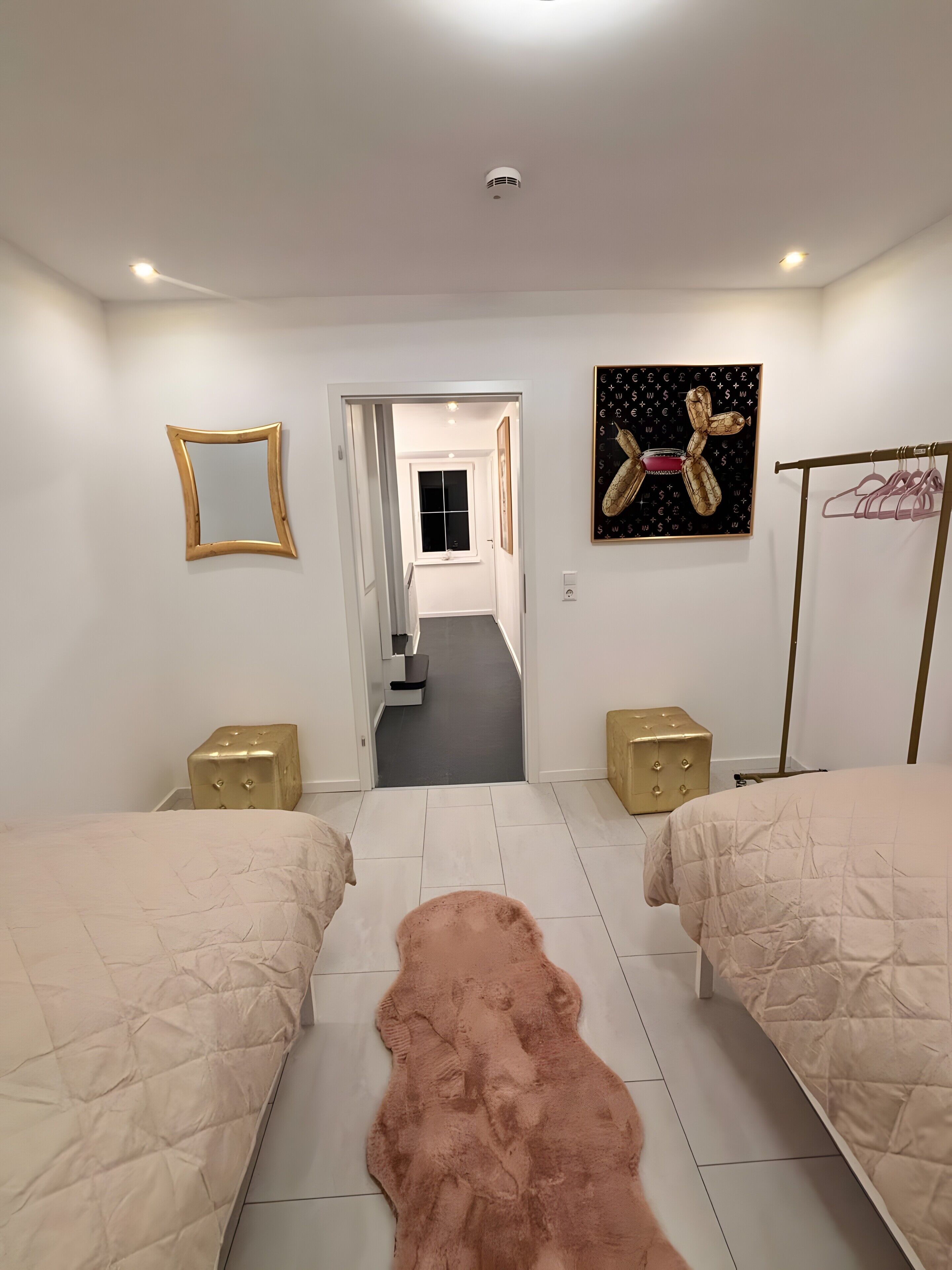 Une chambre avec deux lits, un tapis moelleux, un couloir menant à une autre pièce et une œuvre d’art accrochée au mur.