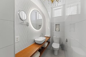 A modern bathroom with a wooden vanity, two mirrors, a white sink, a toilet, and a shower area. - Keizershof, Otrobanda, Stylish Open-Concept Apt 25 (Willemstad)