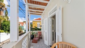 Ein Balkon mit gemustertem Boden, einem Holzstuhl und Blick auf ein gelbes Gebäude.
