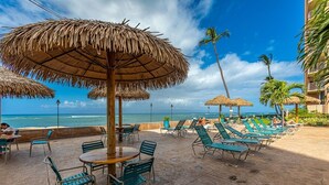 A beachside patio with thatched umbrellas, lounge chairs, and tables, overlooking the ocean. - Royal Kahana 217 Condo (Lahaina)