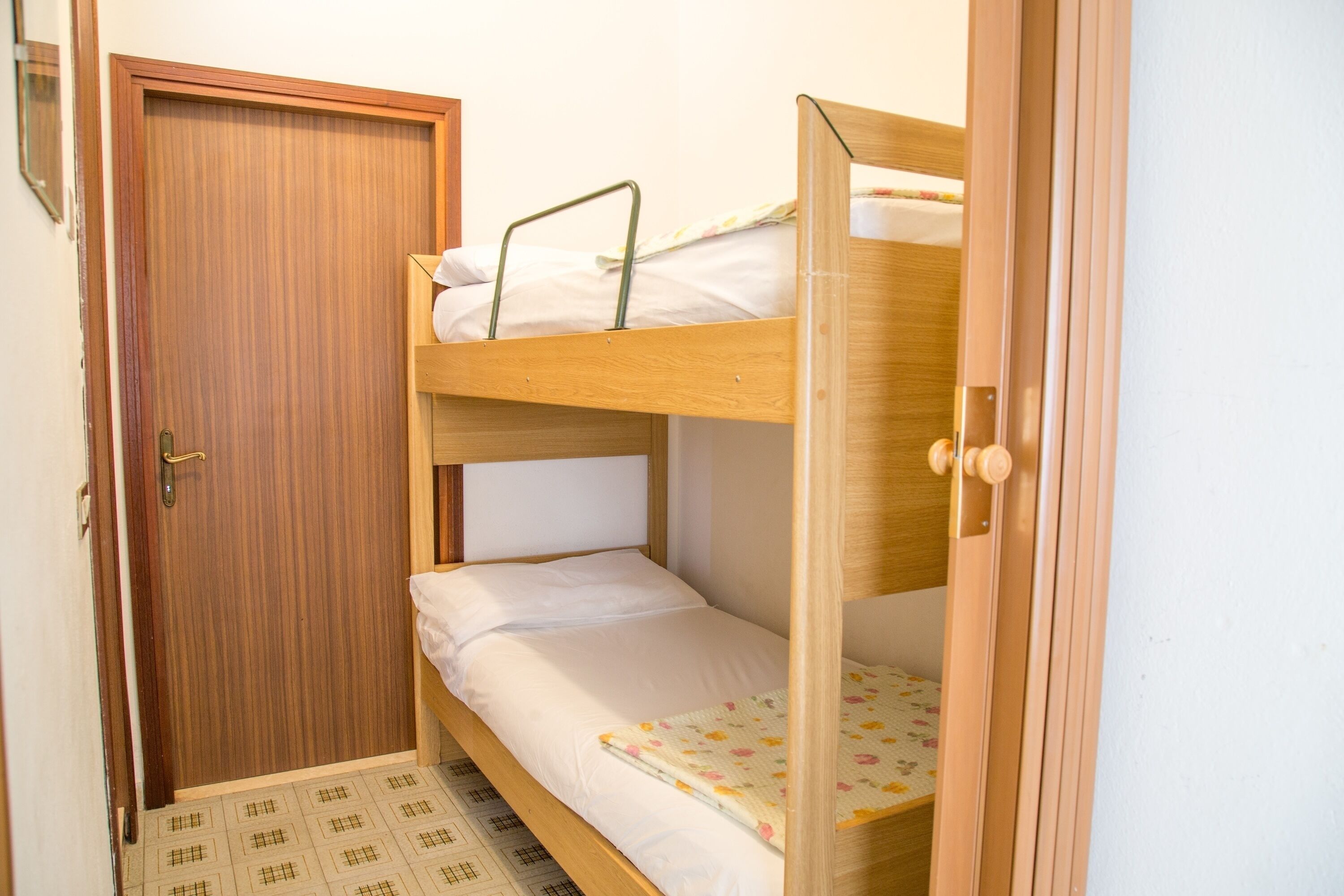Een slaapkamer met stapelbed, een houten deur en een vloermat met patroon.