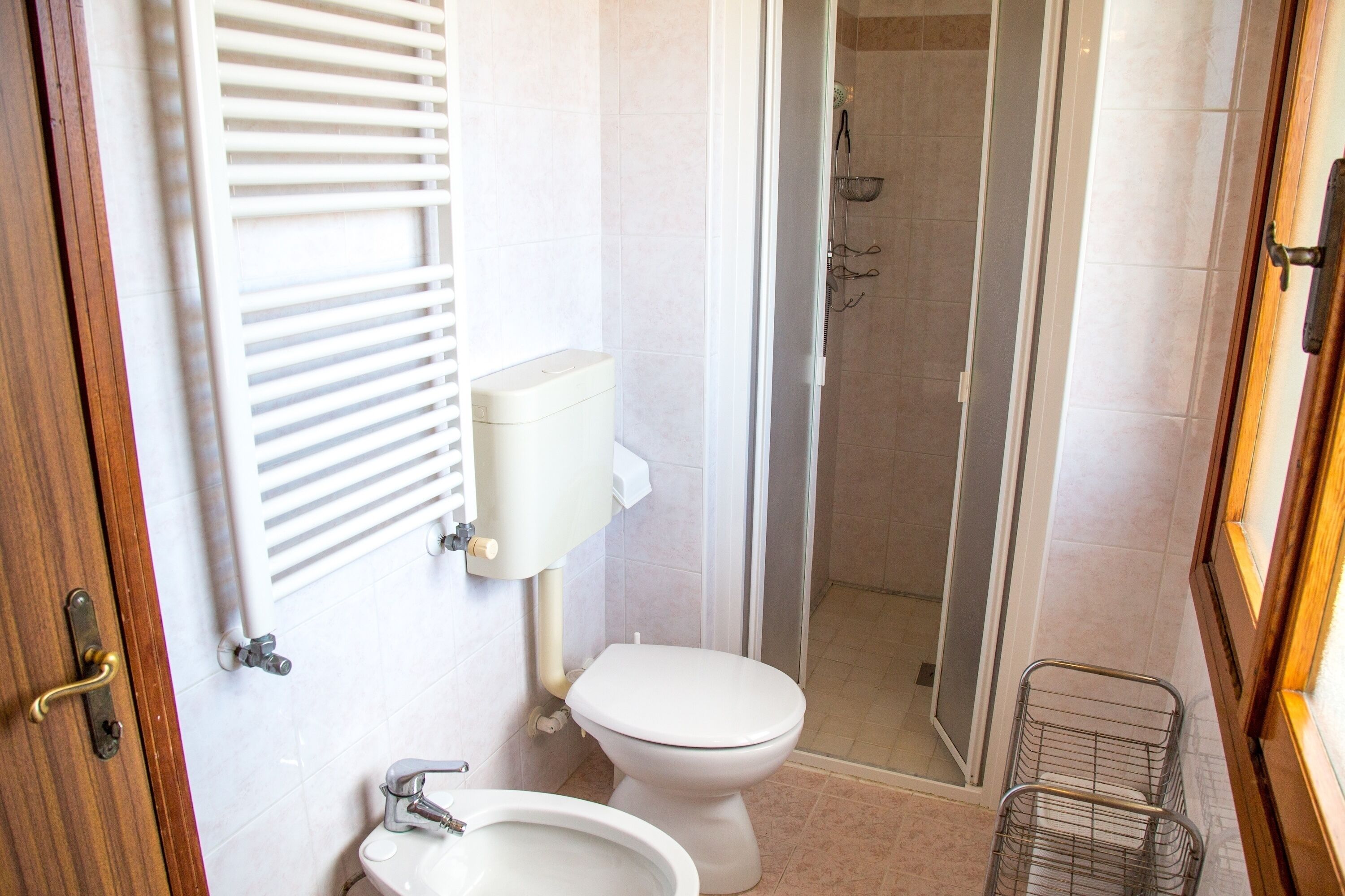 A bathroom with a toilet, sink, shower, and a metal basket.